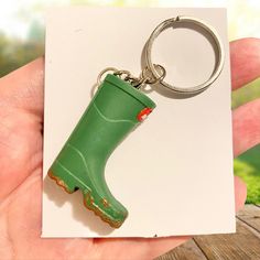 a hand holding a green rubber boot keychain on top of a piece of paper