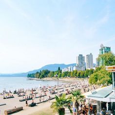 many people are on the beach in front of some buildings and trees with mountains in the background