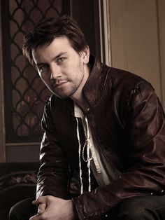 a man in a leather jacket is posing for a photo with his hands on his knees