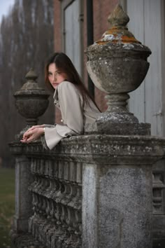 a woman leaning on a stone fence in front of a building