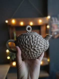 a hand holding a ceramic teapot with lights in the background