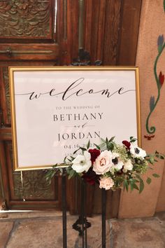 a welcome sign with flowers and greenery on it