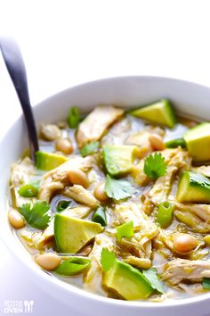 a white bowl filled with chicken, avocado and bean soup next to a spoon