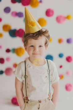 a young boy wearing a party hat and suspenders with confetti on the wall behind him