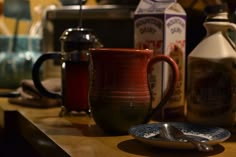 a coffee mug sitting on top of a wooden counter next to bottles and spoons