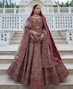 a woman in a red and gold bridal gown standing on steps with her hands behind her back