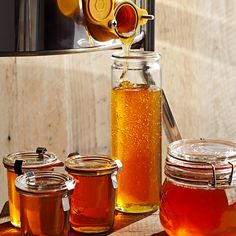 honey is being poured into jars on a wooden table next to an open canister