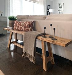 a wooden bench with candles on it in front of a white couch and window sill