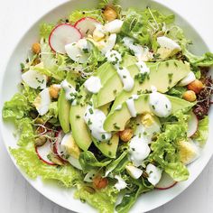 a salad with avocado, radishes and ranch dressing on the side