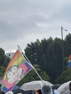 a group of people holding umbrellas and flags in front of some trees with buildings behind them