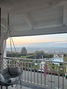 a hanging chair on a porch overlooking the city and hills in the distance with flowers