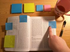 a person holding a pen and looking at an open book with sticky notes on it