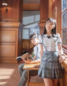 two people are sitting at a desk in front of a window and one is holding a book