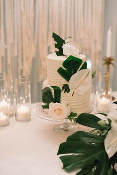 a wedding cake with white flowers and greenery sits on a table surrounded by candles