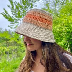 a woman wearing a crocheted hat in front of some trees and grass with the sun shining on her face