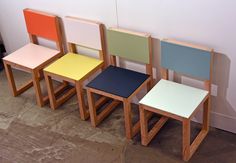 four different colored chairs sitting next to each other on the floor in front of a wall