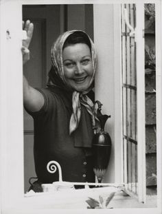 a woman standing in front of a window waving at the camera with her hand up