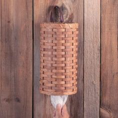 a person is holding up a woven toilet paper roll in front of a wooden wall