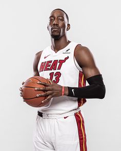 a man holding a basketball in his right hand and wearing a white uniform with red trim