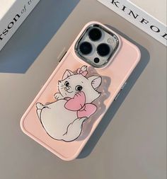 an iphone case with a cartoon cat on the front and back cover, sitting on top of a table next to a book