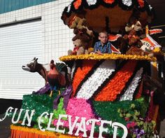 a float with people riding on it in the middle of the street, decorated with flowers and stuffed animals