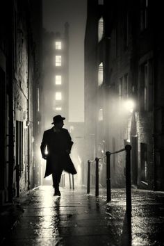 a man walking down a street in the rain at night with an umbrella and hat