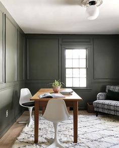 a dining room with green walls and white chairs in front of a wooden table that has a potted plant on top of it