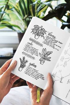 a person holding an open book in their hands with plants on the pages and writing