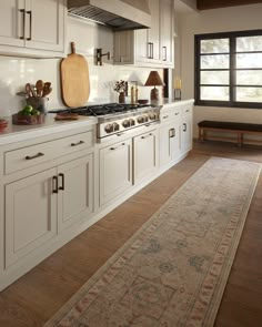 a large kitchen with white cabinets and wooden flooring on the walls, along with an area rug in front of the stove