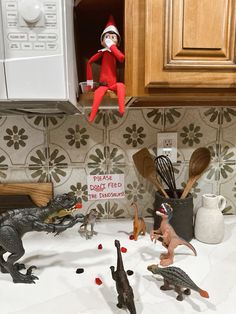 an elf is sitting on the kitchen counter next to toy dinosaurs and cooking utensils