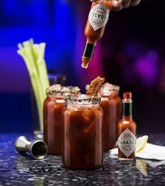 a person is pouring sauce into two glasses with celery sticks on the side