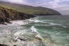 the ocean is choppy with waves coming in to shore and green hills on the far side