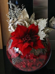 a red poinsettia in a glass bowl with silver decorations on the side