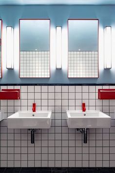 three sinks in a public restroom with mirrors on the wall and red lights above them