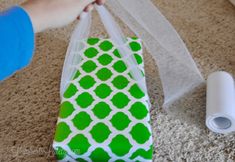 a person holding a green and white gift bag on the floor next to a roll of toilet paper