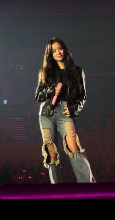 a woman standing on top of a stage wearing ripped jeans and a leather jacket with fringes