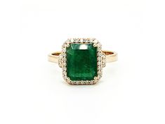 an emerald and diamond ring on a white background, with the center stone surrounded by small diamonds