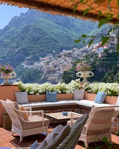 a patio with wicker furniture and flowers on the balcony overlooking a mountain town below