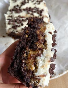 a hand holding a piece of cake with chocolate chips on top and white frosting