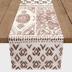 an image of a table runner on top of a wooden table with white and brown designs