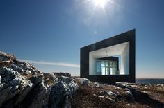 a black building sitting on top of a rocky hill next to the ocean with rocks and grass