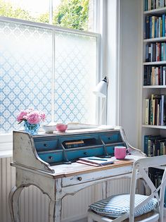 a white desk with a blue top and drawers in front of a window filled with books