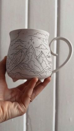 a hand holding a white cup with mountains on it