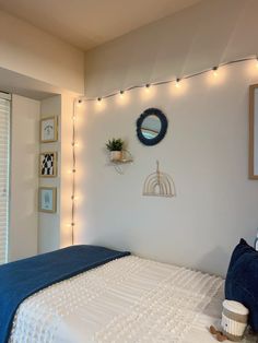 a bedroom with white walls and string lights on the wall above the bed is decorated with blue throw pillows