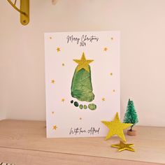 a handmade christmas card with a green tree and yellow stars on the bottom, sitting next to a small pine tree