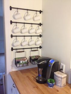 there is a coffee maker on the counter with cups hanging from it's hooks