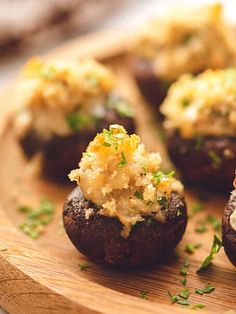 stuffed mushrooms topped with cheese and herbs on a black plate next to some parsley