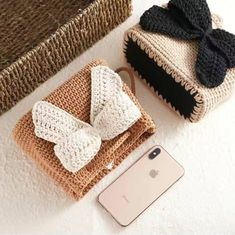 two crocheted purses with bows on them next to an iphone and phone case