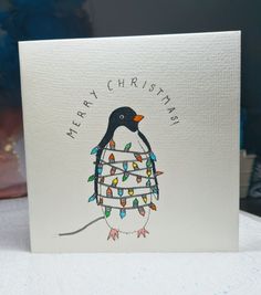 a christmas card with a penguin holding a string of lights on it's chest