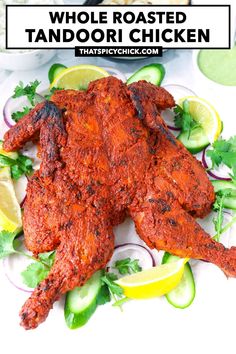 whole roasted tandoori chicken on a plate with cucumbers and lemon wedges